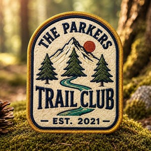 Puede incluir: Un parche bordado con fondo crema y borde amarillo. Presenta una montaña, tres pinos y un río sinuoso. El texto dice THE PARKERS TRAIL CLUB y EST. 2021 en letras azul oscuro con un pequeño sol de color naranja.