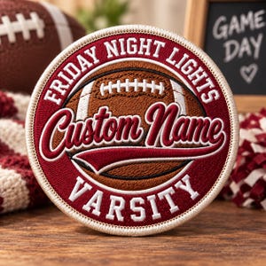 May include: A circular embroidered patch featuring a brown football graphic in the centre. The text "FRIDAY NIGHT LIGHTS" is arched at the top, "Custom Name" is written in a script font across the middle, and "VARSITY" is at the bottom.