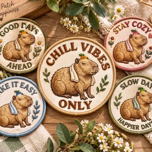 May include: Five circular embroidered patches featuring capybaras with towels and fruit on their heads. The patches include text: Good Days Ahead, Chill Vibes Only, Take It Easy, Stay Cozy, and Slow Days Happier Days, surrounded by floral accents.