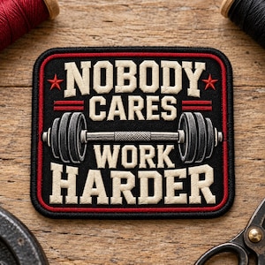 May include: A square embroidered patch with a black background and a red border. The text reads NOBODY CARES WORK HARDER in beige block letters. A grey barbell with black weight plates is centred between the lines of text, flanked by two small red stars.