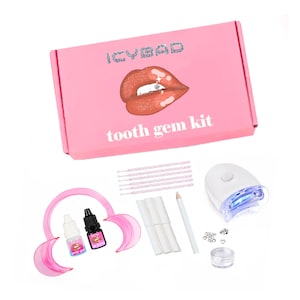 Könnte beinhalten: Eine rosa Box mit der Aufschrift "ICYBAD" und "tooth gem kit" und einem Lippen-Design. Das Set enthält Werkzeuge für das Anbringen von Zahnschmuck: Mundöffner, Prep-Gel- und Klebeflaschen, Applikatoren, Bleistift, Wattepads, Aushärtelampe und Schmucksteine.