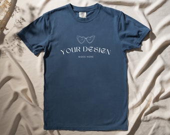 May include: A blue t-shirt with a white graphic of sunglasses and the text "YOUR DESIGN GOES HERE".