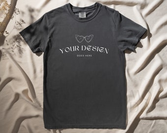May include: A dark gray t-shirt with a white graphic of a pair of heart-shaped sunglasses and the text "YOUR DESIGN GOES HERE".