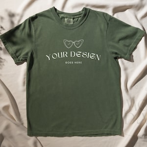 Op de afbeelding: Een groen T-shirt met een witte afbeelding van een zonnebril en de tekst "YOUR DESIGN GOES HERE".