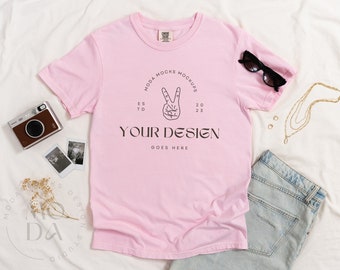 May include: A pink t-shirt with a peace sign graphic and the text "MODA MOCKS MOCKUPS ES TD 20 23 YOUR DESIGN GOES HERE".