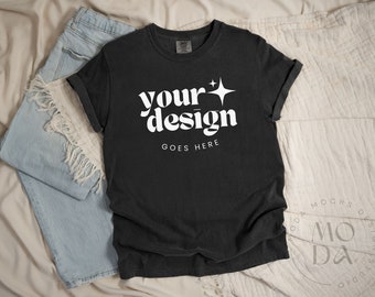 May include: Black t-shirt with white text that says "your design goes here" and a small white star. The shirt is laying on a white and blue fabric background.