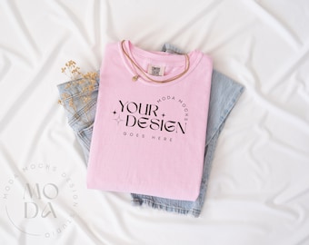 May include: Pink t-shirt with a black graphic that says "YOUR DESIGN GOES HERE" and a gold chain necklace. The shirt is folded on top of a pair of blue jeans.