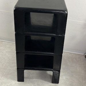 May include: A set of four black plastic nesting tables with a unique design. Each table has a square top and a rectangular opening on the front. The tables are stacked on top of each other.