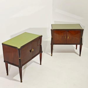 May include: Two matching wooden cabinets with a glossy, dark brown finish. Each cabinet has a light green top, two doors, and four slender legs. Gold-colored hardware and accents add a touch of elegance to the design. The cabinets are placed against a white background.