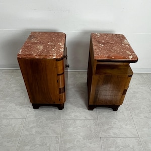 May include: A pair of vintage wooden nightstands with marble tops. The nightstands have a curved design and feature a drawer and a shelf. The marble tops are a light pink color with white veining.