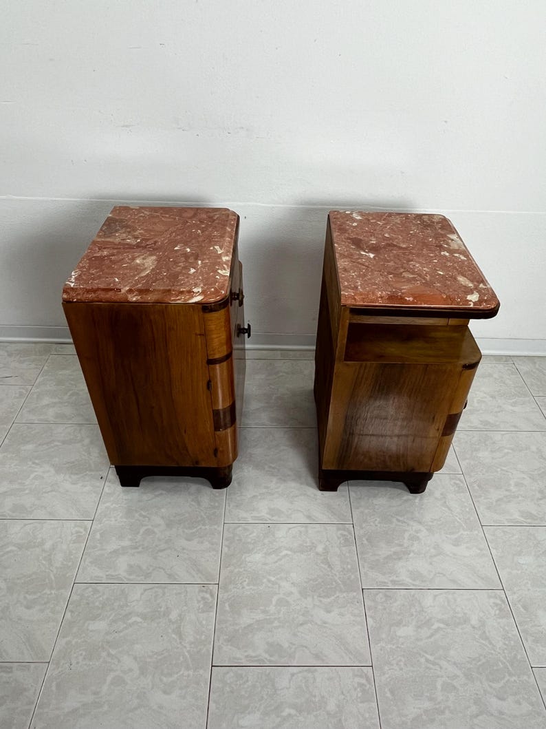 May include: A pair of vintage wooden nightstands with marble tops. The nightstands have a curved design and feature a drawer and a shelf. The marble tops are a light pink color with white veining.