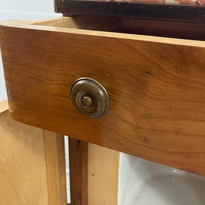 May include: A wooden cabinet with a single drawer and a door. The drawer has a brass knob and the cabinet has a marble top.