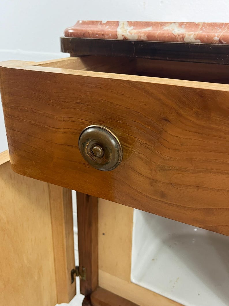 May include: A wooden cabinet with a single drawer and a door. The drawer has a brass knob and the cabinet has a marble top.
