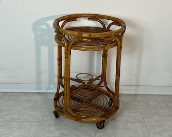 May include: A round, brown bamboo bar cart with two shelves and wheels. The cart has a woven design and is perfect for serving drinks.