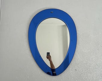 Puede incluir: Espejo de pared ovalado con un marco azul vibrante. El marco del espejo tiene un acabado liso y brillante. El espejo está colgado en una pared blanca texturizada.