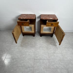 May include: Two matching wooden nightstands with a drawer and a door. Each nightstand has a pink marble top and a light wood finish.