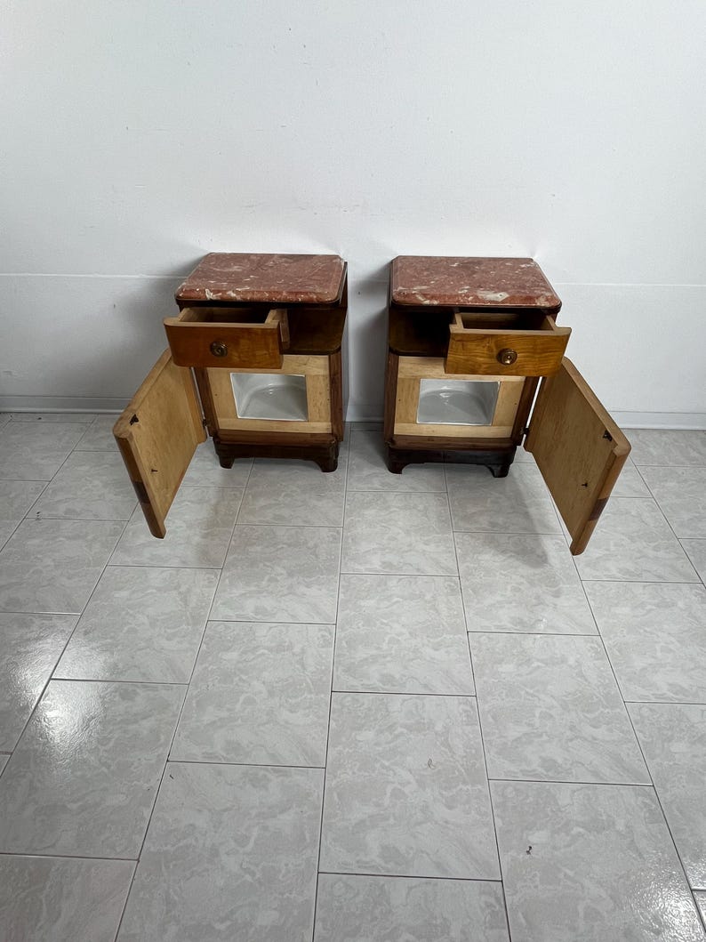 May include: Two matching wooden nightstands with a drawer and a door. Each nightstand has a pink marble top and a light wood finish.