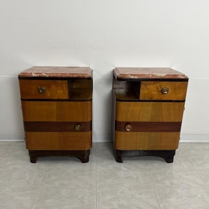 May include: A pair of vintage wooden nightstands with marble tops. Each nightstand has two drawers and a small shelf. The nightstands are in good condition and have a warm, honey-colored finish.