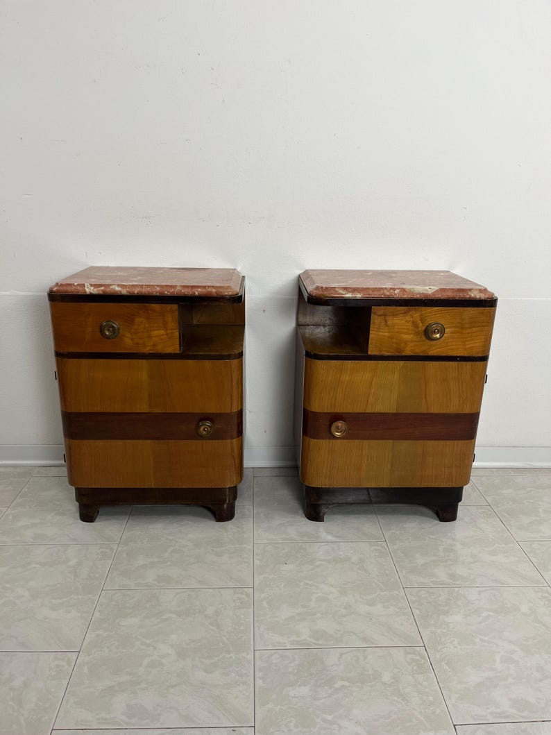 May include: A pair of vintage wooden nightstands with marble tops. Each nightstand has two drawers and a small shelf. The nightstands are in good condition and have a warm, honey-colored finish.