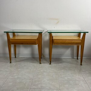 May include: A pair of mid-century modern nightstands with glass tops and a single drawer. The nightstands are made of wood and have brass legs.
