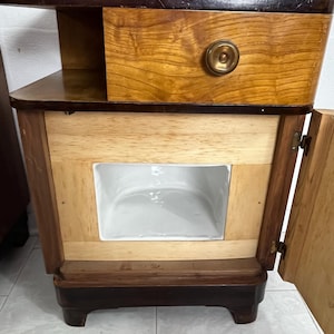 May include: A corner cabinet with a marble top, a wooden drawer with a brass knob, and a wooden door with a brass hinge. The cabinet has a white porcelain interior.