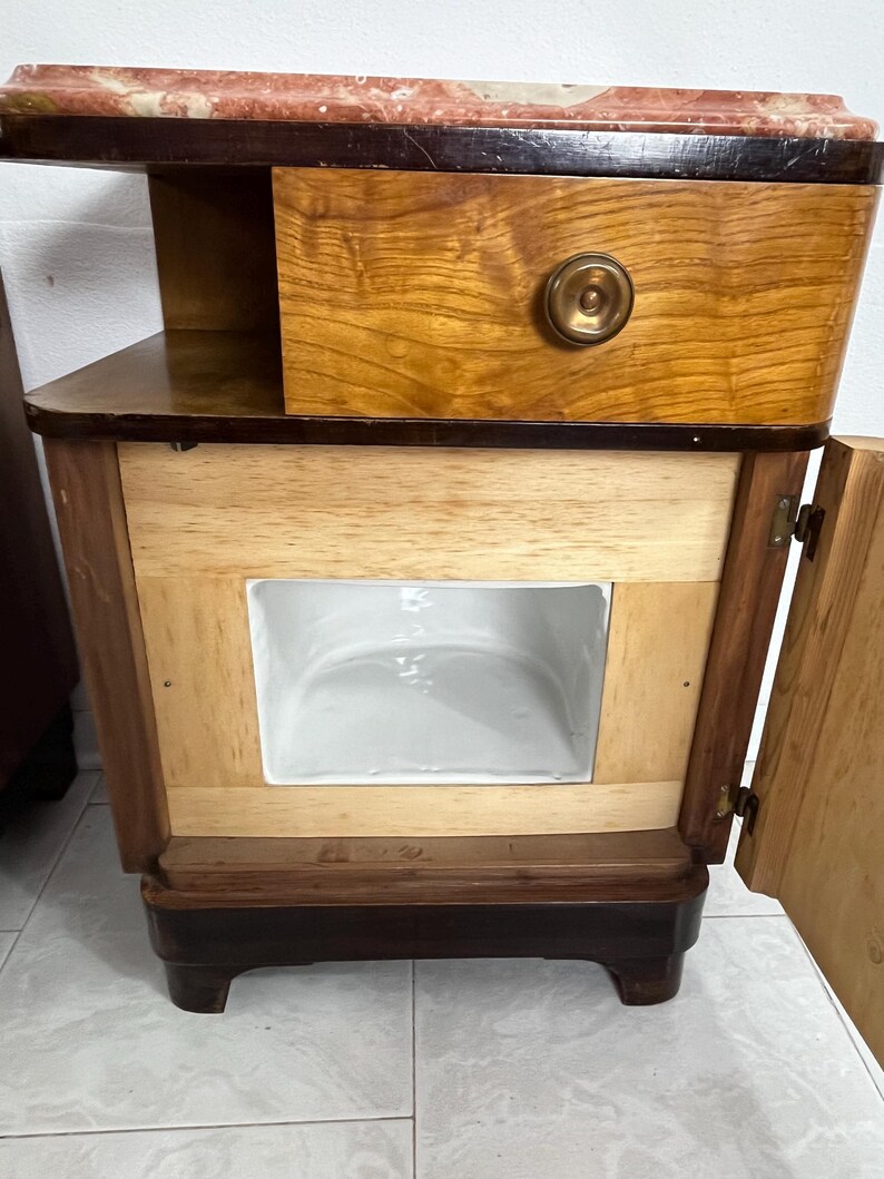 May include: A corner cabinet with a marble top, a wooden drawer with a brass knob, and a wooden door with a brass hinge. The cabinet has a white porcelain interior.