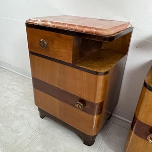 May include: A pair of vintage wooden nightstands with a marble top. Each nightstand has two drawers and a small shelf. The nightstands are in a light wood tone with dark wood accents.