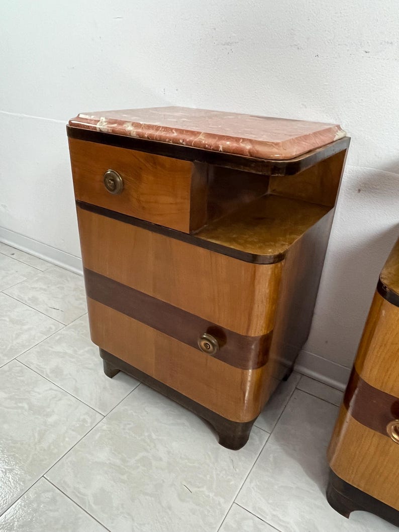May include: A pair of vintage wooden nightstands with a marble top. Each nightstand has two drawers and a small shelf. The nightstands are in a light wood tone with dark wood accents.