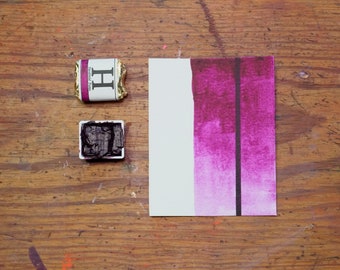 Può includere: Una pastiglia di acquerello con un pigmento viola scuro e un'etichetta che recita "Winsor & Newton,  H,  Handmade Paints". Un lavaggio ad acquerello viola è dipinto su un foglio di carta bianco.
