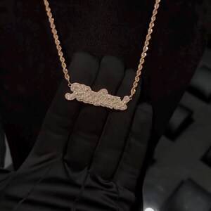 May include: A gold chain necklace with a diamond-encrusted pendant in the shape of a word. The pendant is a popular style for personalized jewelry.