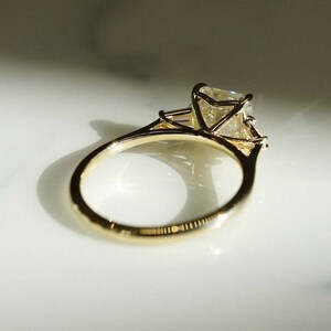 May include: A gold engagement ring with a large, clear, square-shaped diamond set in a prong setting. The ring has a simple band.