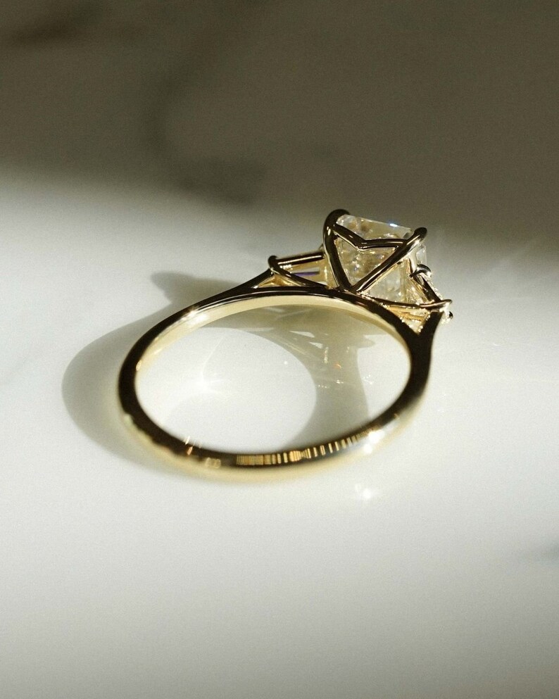 May include: A gold engagement ring with a large, clear, square-shaped diamond set in a prong setting. The ring has a simple band.
