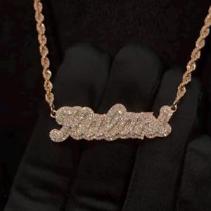 May include: A gold chain necklace with a diamond-encrusted pendant that spells out the name "Jalena".