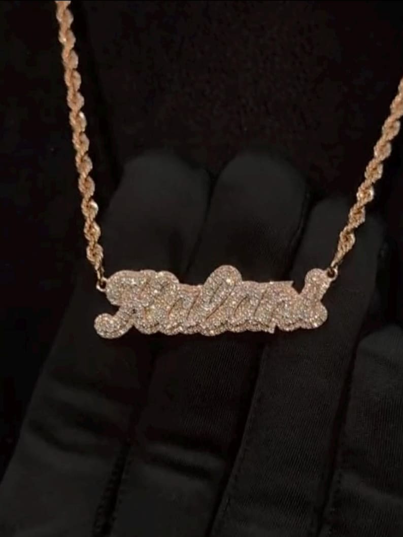 May include: A gold chain necklace with a diamond-encrusted pendant that spells out the name "Jalena".