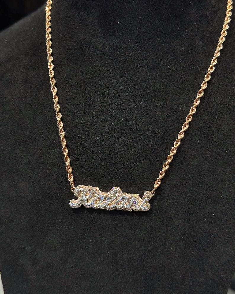 May include: A gold rope chain necklace with a diamond-encrusted nameplate pendant that reads "Kalan."