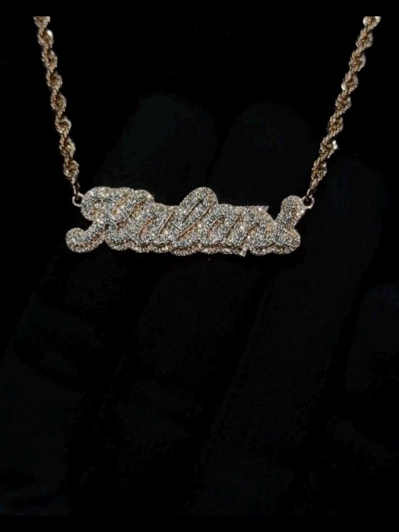 May include: A gold chain necklace with a diamond-encrusted pendant spelling out the name "Julia".
