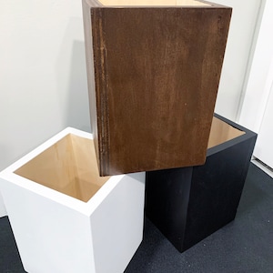 May include: Three square wooden storage boxes in different colors: white, brown, and black. The boxes are stacked on top of each other.