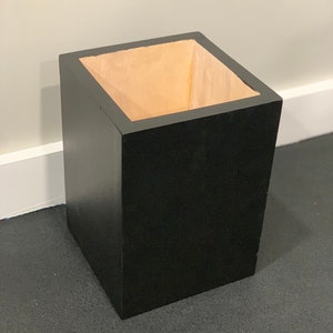 May include: A black square-shaped trash can with a wooden interior.