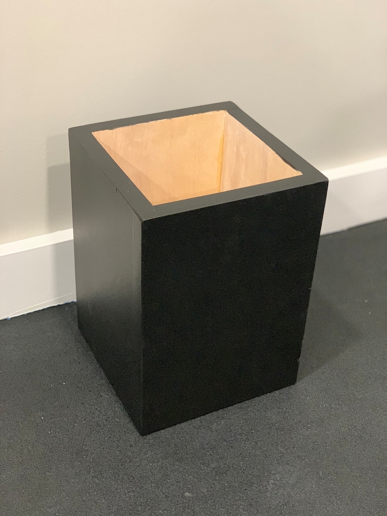 May include: A black square-shaped trash can with a wooden interior.