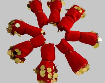 May include: A circular arrangement of seven red fabric wraps, each featuring a decorative border of shiny gold-colored circular sequins. The wraps are rolled into cylindrical shapes, showcasing the vibrant red textile and the metallic gold accents.