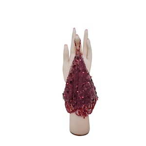 May include: A burgundy sequined evening bag with a beaded handle and fringe. The bag is displayed on a mannequin hand against a white background. The sequins and beads add a touch of glamour.