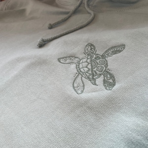 A delicate turtle embroidered in a complimentary colour on the left chest of the hoodie which is available in a choice of 9 colours, see colour chart for more details