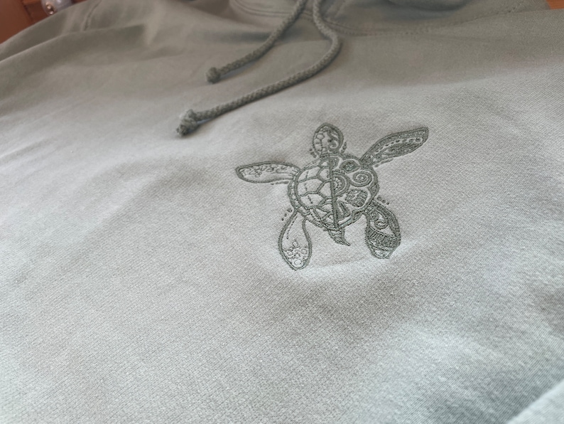 A delicate turtle embroidered in a complimentary colour on the left chest of the hoodie which is available in a choice of 9 colours, see colour chart for more details
