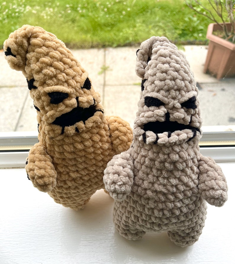 May include: Two crocheted plush toys shaped like the character Oogie Boogie from the movie The Nightmare Before Christmas. One is tan and the other is gray.