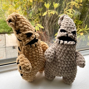 May include: Two crocheted plush toys in the shape of the Nightmare Before Christmas characters, Oogie Boogie and Lock, Shock, and Barrel. The Oogie Boogie plush is brown and the Lock, Shock, and Barrel plush is gray.