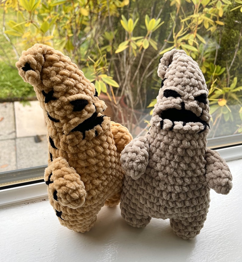 May include: Two crocheted plush toys in the shape of the Nightmare Before Christmas characters, Oogie Boogie and Lock, Shock, and Barrel. The Oogie Boogie plush is brown and the Lock, Shock, and Barrel plush is gray.
