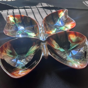 May include: A butterfly-shaped ceramic dish featuring a glossy glaze with a blend of deep black, burnt orange, and vibrant teal colours. The four-sectioned bowl has curved, organic edges and a smooth, reflective surface throughout the entire piece.