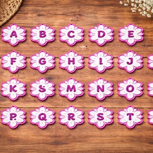 May include: A collection of twenty-one flower-shaped alphabet letters, each with a white center and a pink border. The letters A through V are displayed on a wooden surface, perfect for crafting or educational projects.