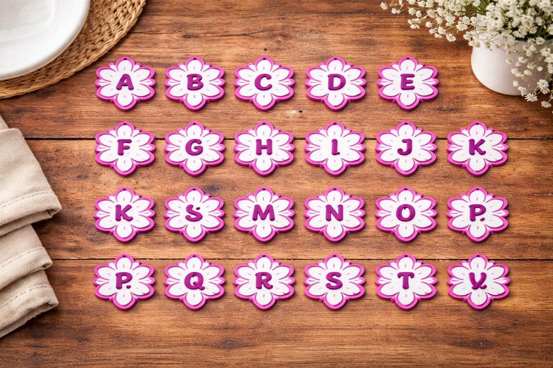 May include: A collection of twenty-one flower-shaped alphabet letters, each with a white center and a pink border. The letters A through V are displayed on a wooden surface, perfect for crafting or educational projects.