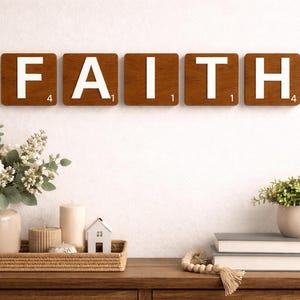 Six brown Scrabble tiles spell "FAITH" horizontally on a white wall above a wooden console table with decor.